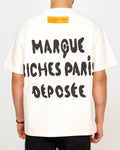 Back view of a men’s oversized white T-shirt featuring bold black Riches Paris typography and a contrast neck patch.