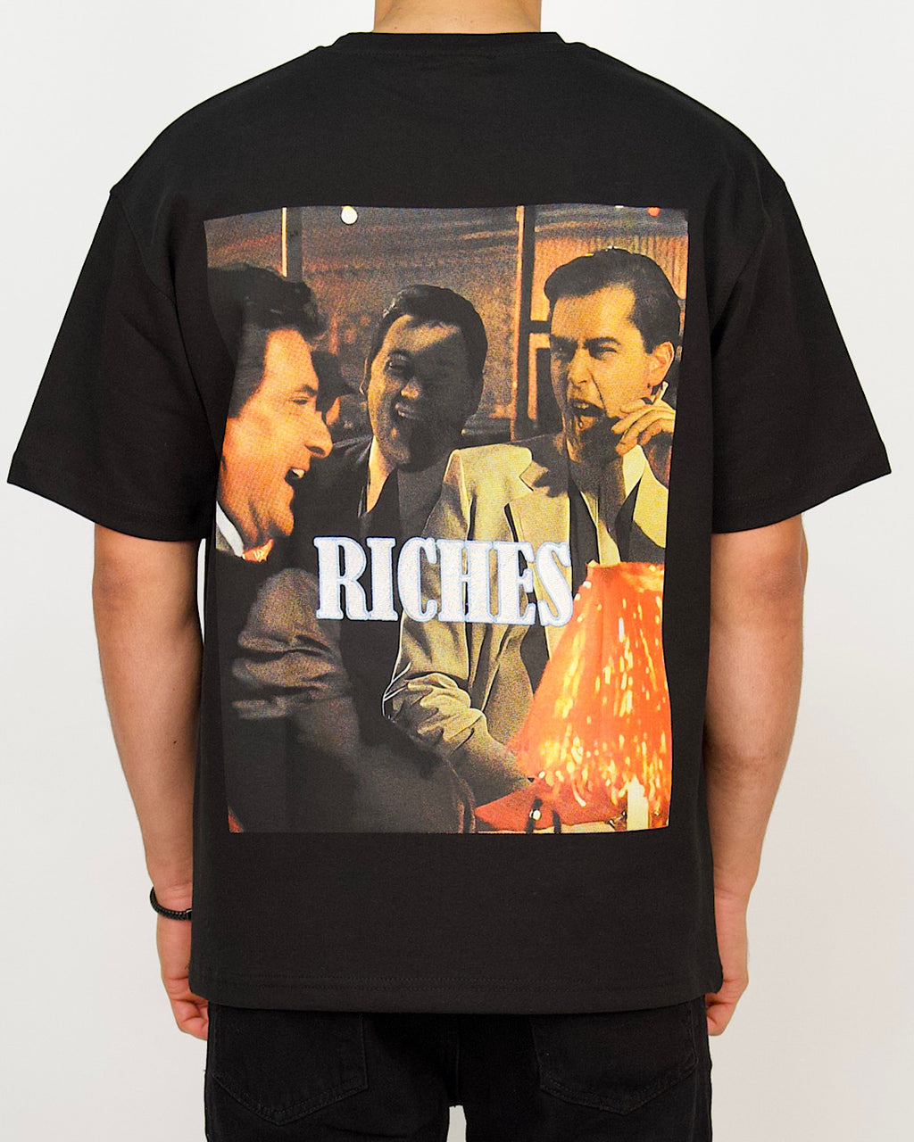 Back view of a men’s oversized black T-shirt featuring a vintage lounge-scene photo print with bold “RICHES” branding.