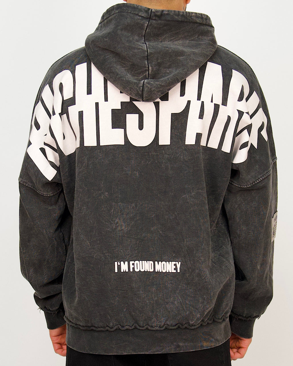 Back view of a men’s oversized washed black hoodie featuring a large Riches Paris back print and “I’M FOUND MONEY” text.