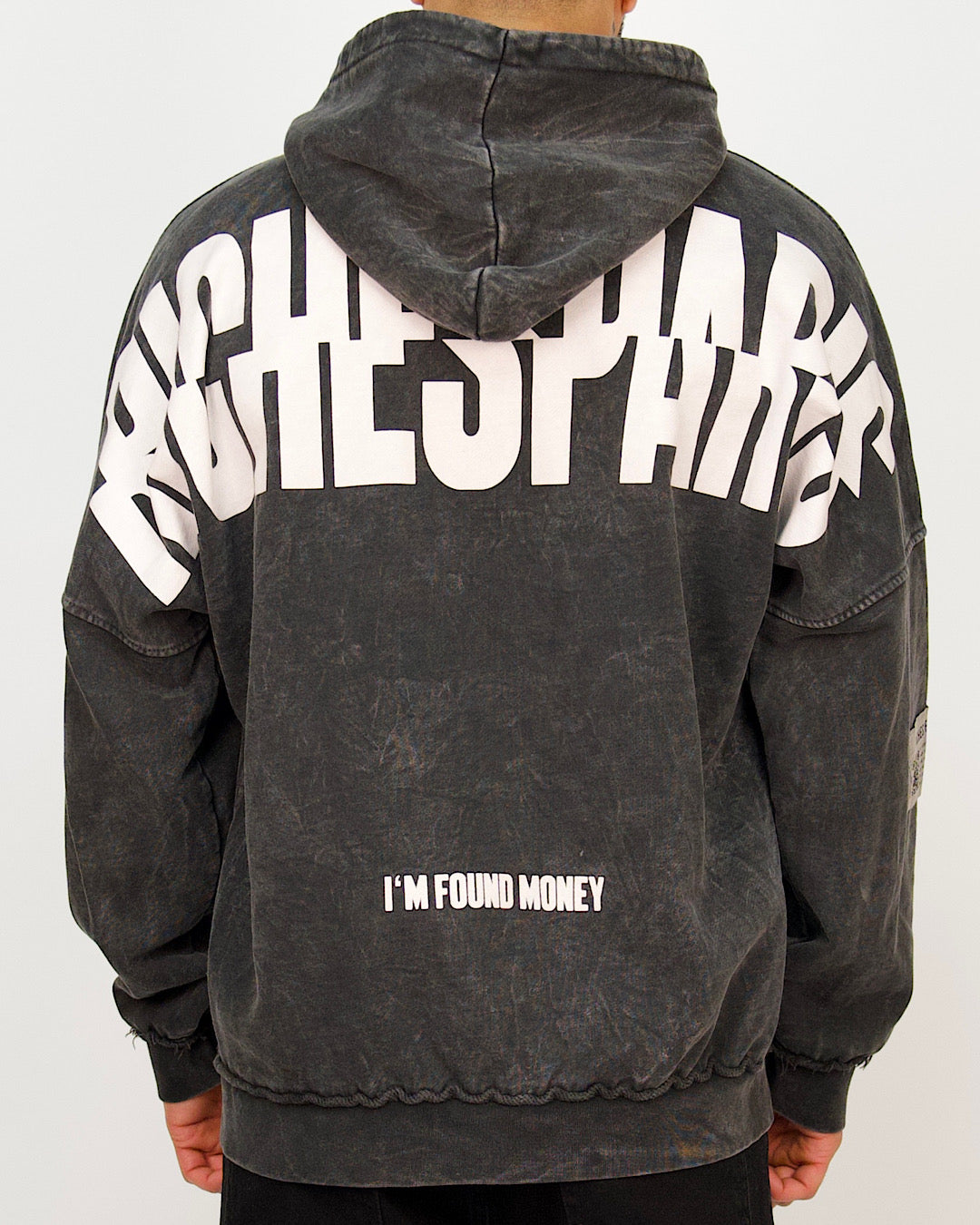 Back view of a men’s oversized washed black hoodie featuring a large Riches Paris back print and “I’M FOUND MONEY” text.