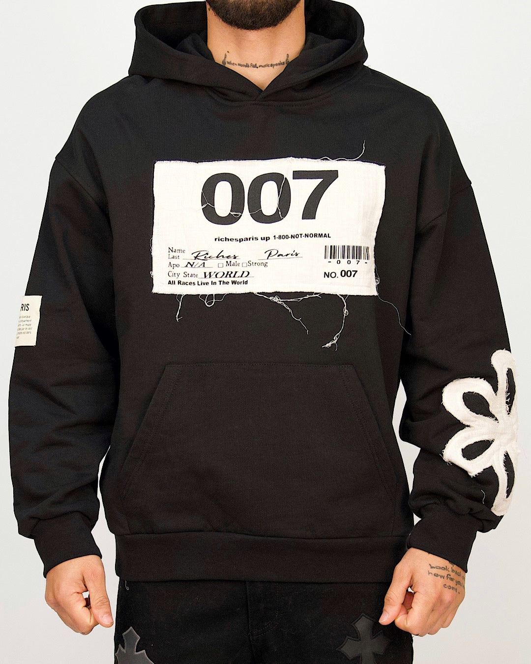 Front view of a men’s oversized black hoodie featuring a distressed 007 patch and textured white appliqué detailing on the sleeve.