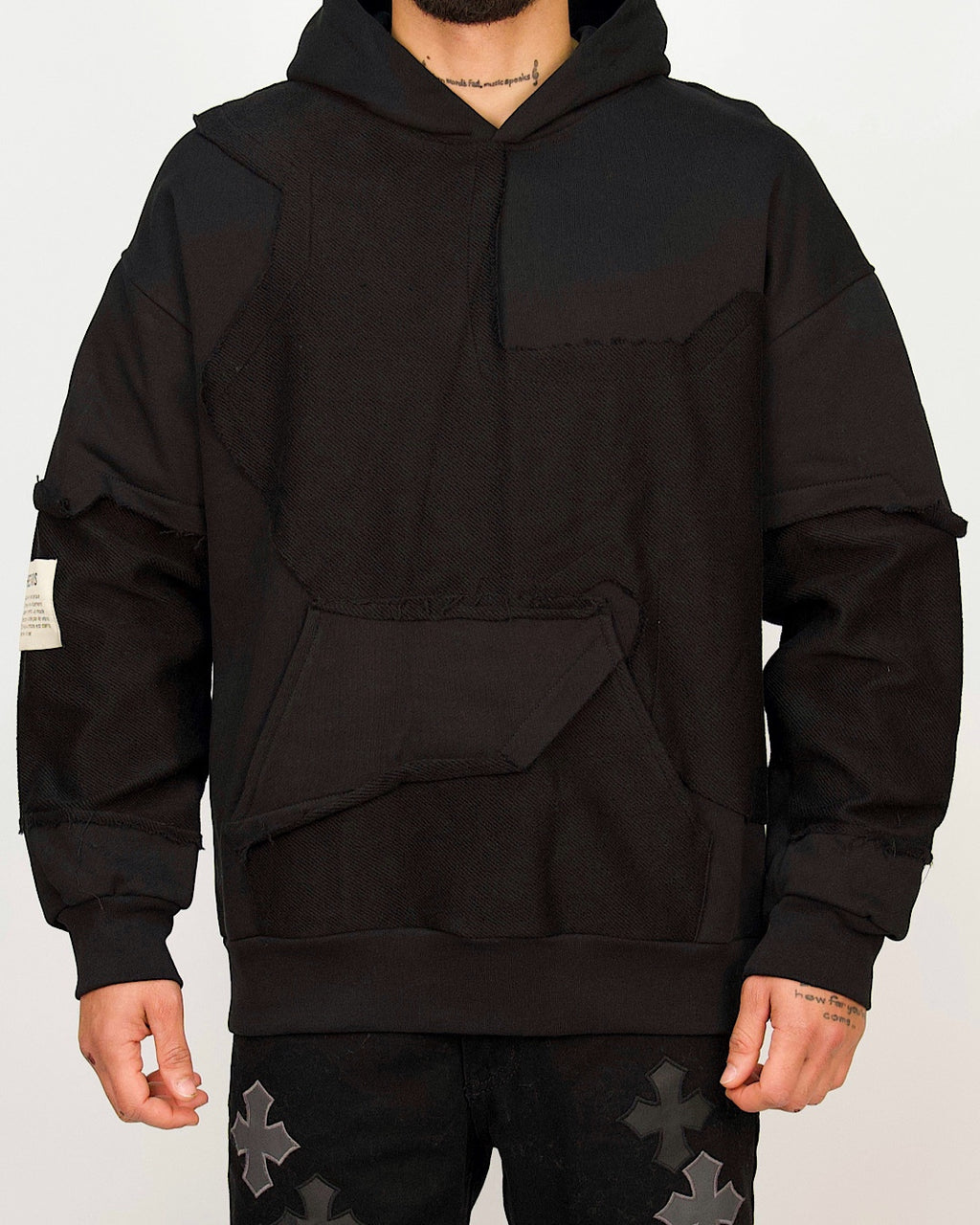 Front view of a men’s oversized black hoodie featuring raw-edged multi-panel construction and a sculpted kangaroo pocket.