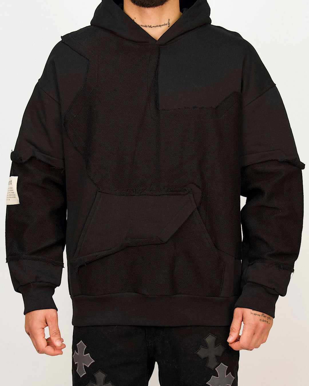 Front view of a men’s oversized black hoodie featuring raw-edged multi-panel construction and a sculpted kangaroo pocket.