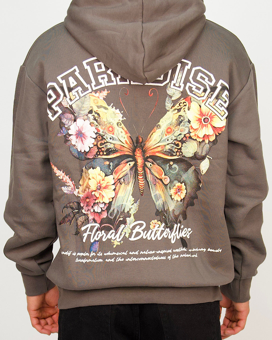 Back view of a men’s oversized anthracite hoodie featuring a large floral butterfly graphic and varsity-style “Paradise” lettering.