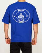 Back view of a men’s oversized blue T-shirt featuring a circular Paris landmark graphic with “Atelier Éternel” text.